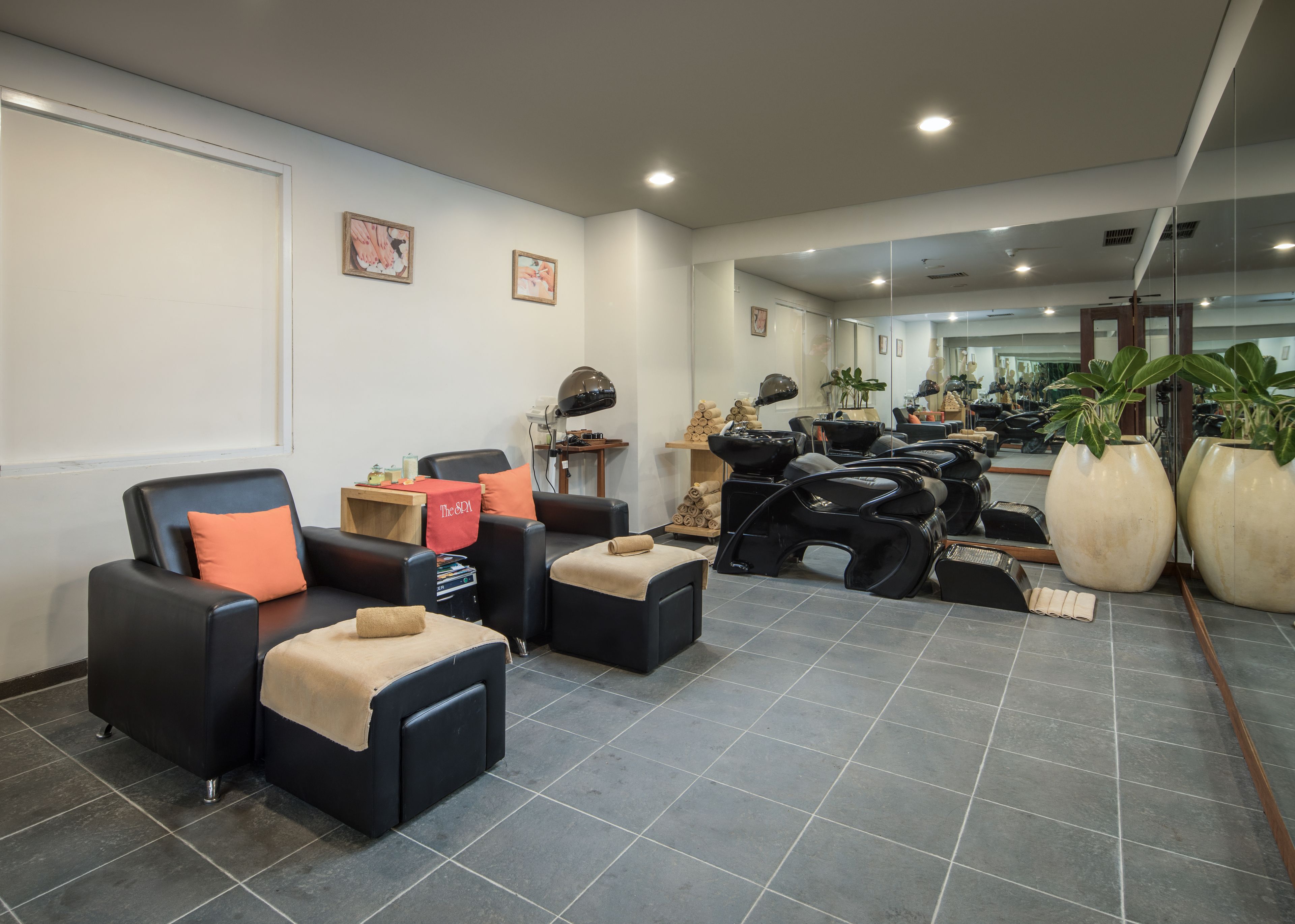 Un spa moderno con sillones de cuero negro, una camilla de masaje y grandes plantas en macetas.