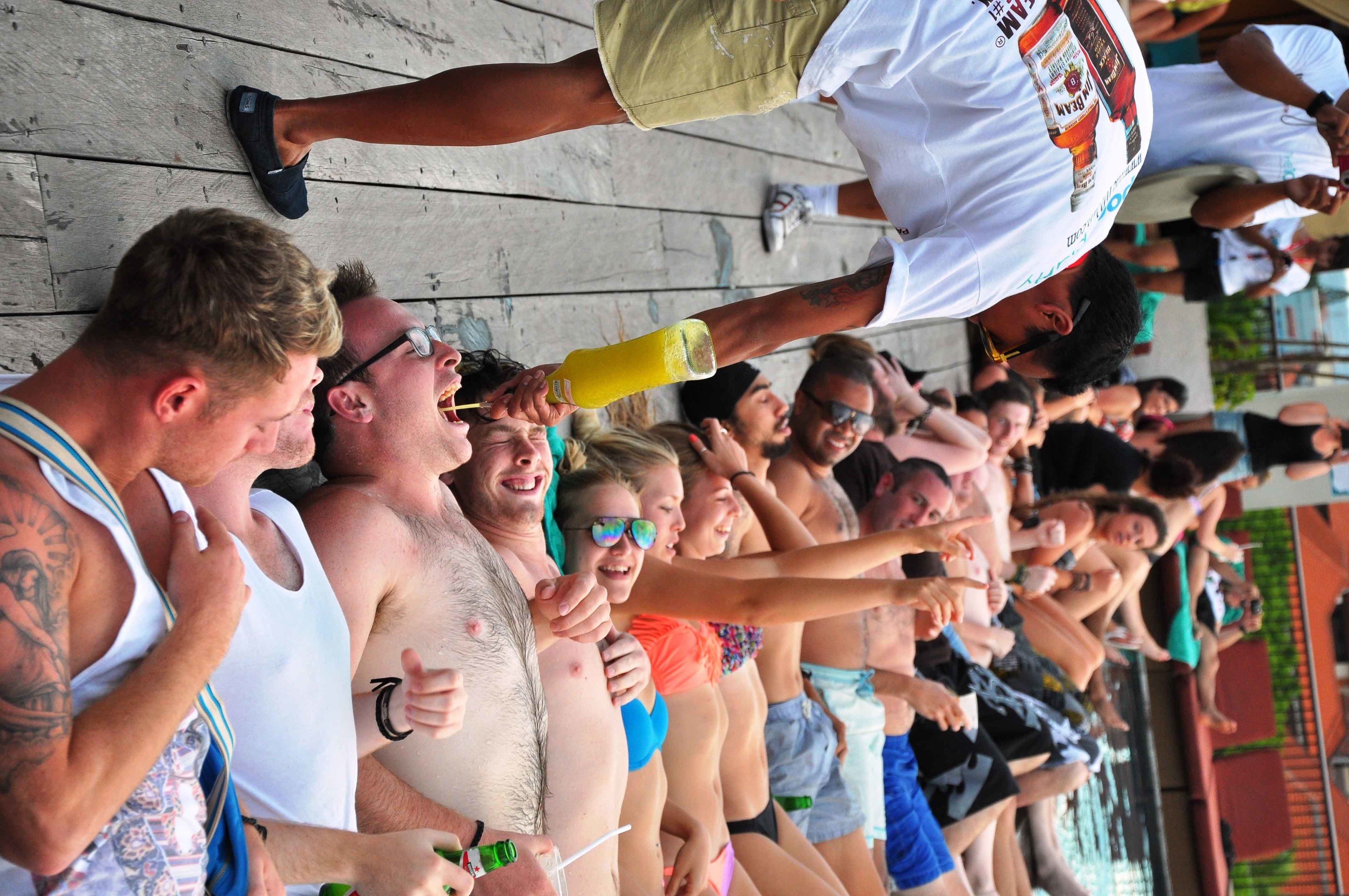 A group of people standing on a wooden deck, some holding drinks.