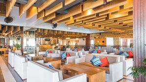 A modern lounge area with white wicker furniture, wooden tables, and red and blue striped pillows.