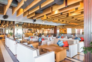 A modern lounge area with white wicker furniture, wooden tables, and red and blue striped pillows.