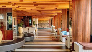 A spacious lobby with a modern wooden ceiling, a central staircase, and seating areas.