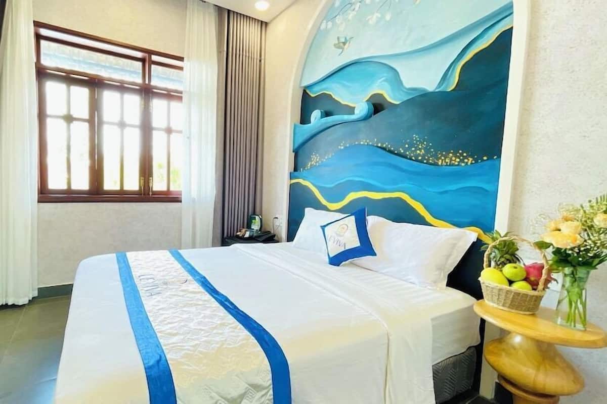 A hotel room with a large bed, a nightstand, a vase with flowers, and a painting on the wall.