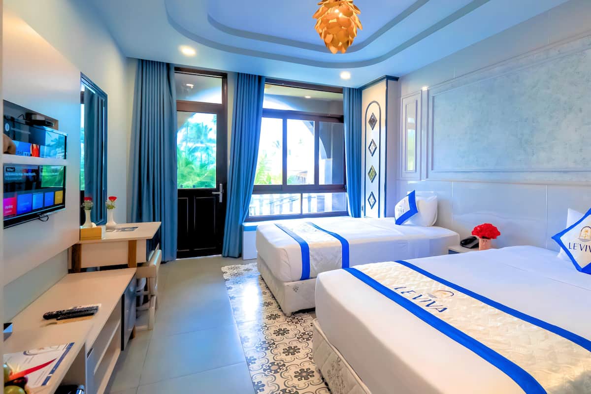 A hotel room with a large bed, a desk, a TV, and a balcony with curtains.
