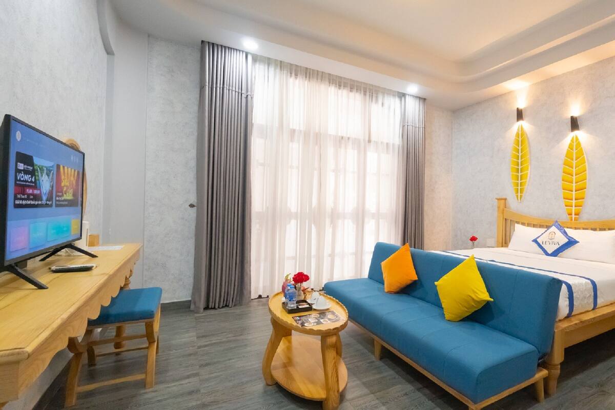 A hotel room with a bed, a desk with a TV, a blue sofa, and a small round table.