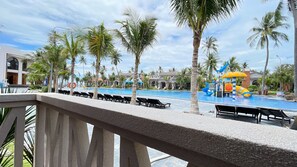 Un área de piscina en un complejo turístico, con sillas de descanso, palmeras y un tobogán de agua.