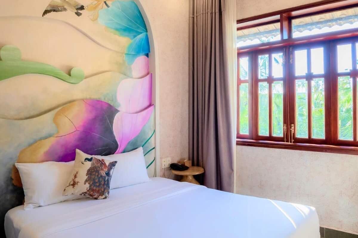A hotel room with a bed, a small table, a telephone, and a window with curtains.