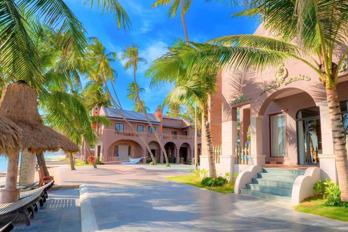 A resort with a pool, palm trees, and a building with arched walkways.