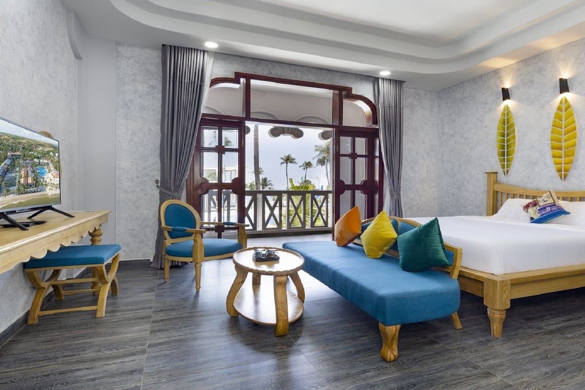A hotel room with a bed, a sofa, a TV, and a balcony with curtains.