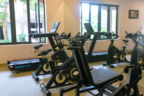 A gym with stationary bikes and treadmills, large windows, and a tiled floor.