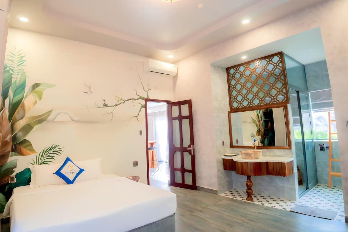 A modern hotel room with a large bed, a bathroom with a mirror and sink, and a view of the outdoors.