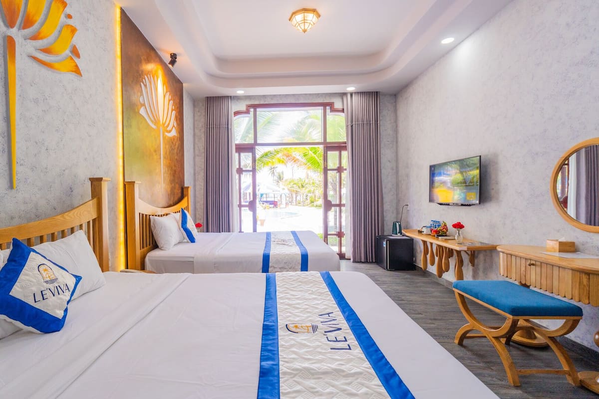 A hotel room with two beds, a TV, a desk, and a view of the outdoors.