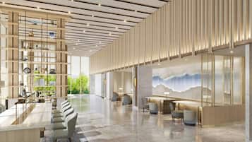 A spacious hotel lobby with a high ceiling, a long reception desk, multiple seating areas, and a large wall mural.