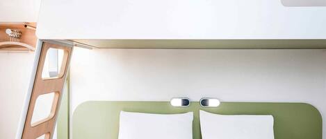 Uma cama beliche com cabeceira verde, uma escada de madeira e uma mesa de cabeceira com uma garrafa e óculos de sol.