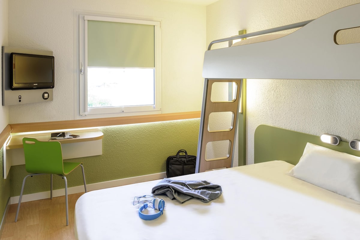 Ein Schlafraum mit Etagenbetten, einem Schreibtisch, einem Stuhl, einem Fernseher und einem Fenster.