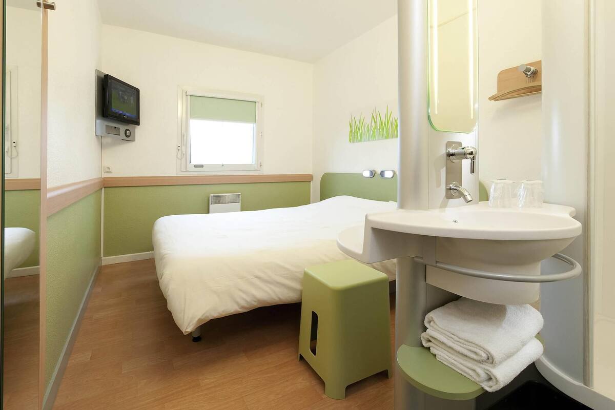 Une chambre d’hôtel comprenant un lit, une table de chevet, un lavabo, un miroir et un téléviseur.