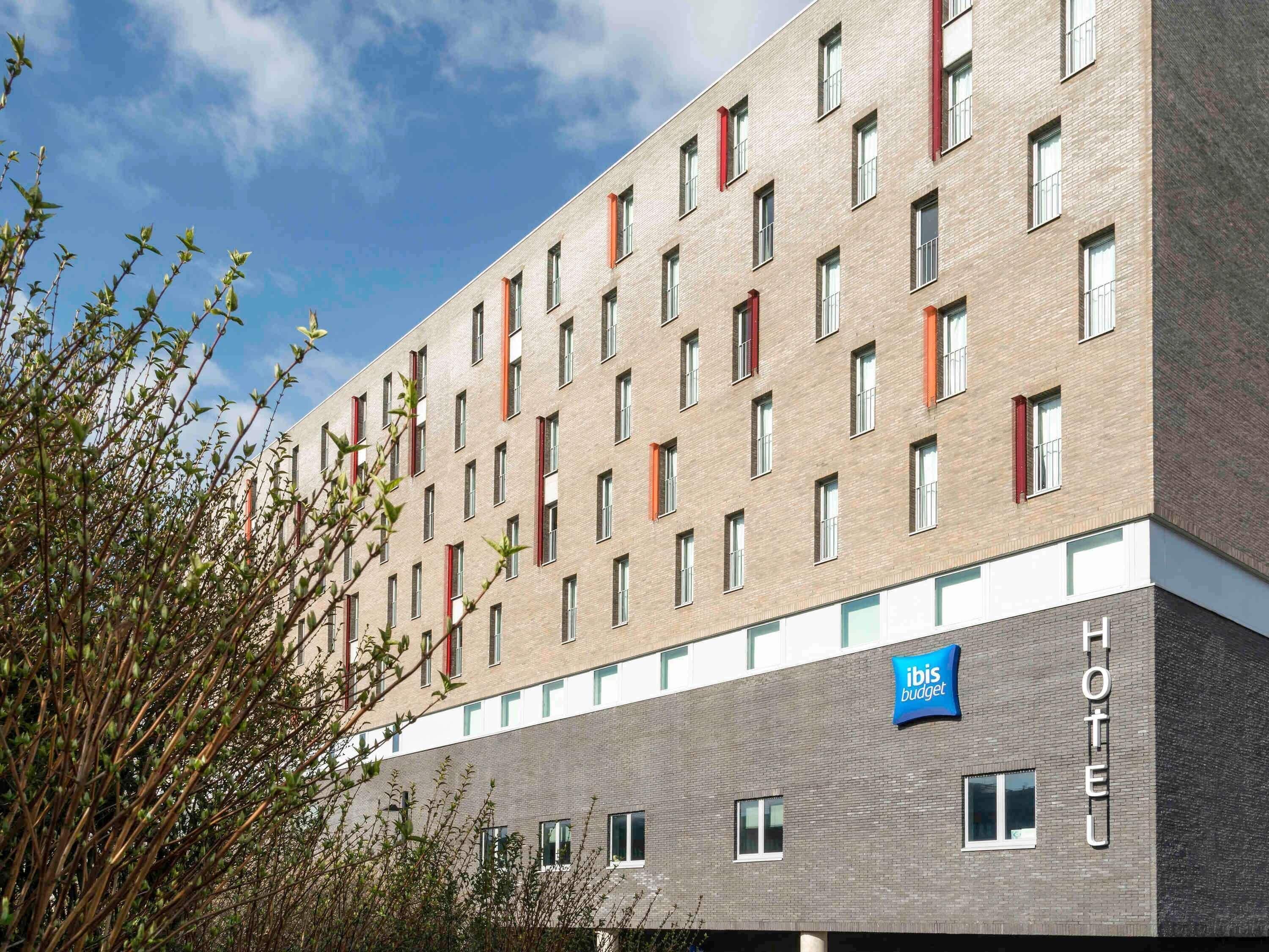 Un edificio de hotel de varios pisos con fachada de ladrillo moderno, numerosas ventanas y un cartel que indica que es un hotel ibis budget.