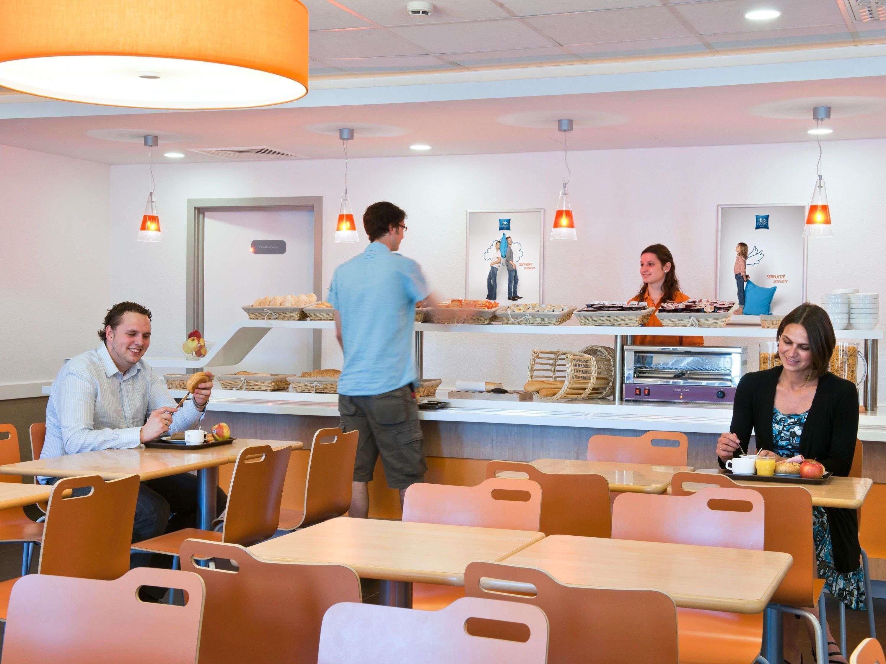 Een cafetaria met tafels en stoelen, een etalage met eten en een persoon die eten serveert.