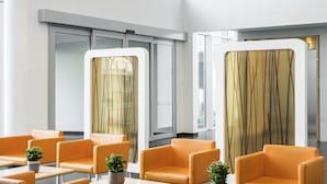 Un espace d’attente moderne avec des chaises et des tables orange, de grandes lampes suspendues orange et une vue sur l’extérieur grâce à de grandes fenêtres.