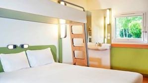 Une chambre d’hôtel comprenant un lit, une table de chevet, une fenêtre donnant sur des arbres et une salle de bain avec un lavabo et un miroir.