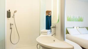 Un baño con ducha, lavabo y cama con pared verde y ropa de cama blanca.