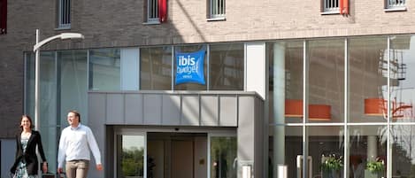 Un edificio moderno con fachada de vidrio, un letrero de ibis budget hotels y un área verde al frente.