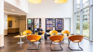Un hall d’entrée moderne avec des fauteuils orange, un distributeur automatique et une personne assise.