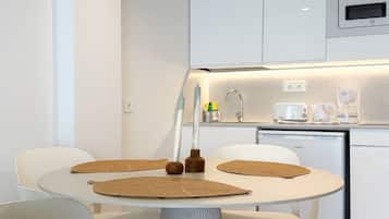 Una cocina moderna con armarios blancos, microondas integrado y un comedor con una mesa redonda y sillas blancas.