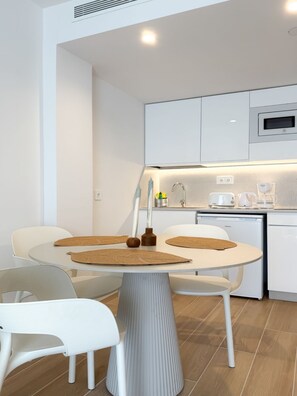 A modern kitchen with white cabinetry, a built-in microwave, and a dining area with a round table and white chairs.