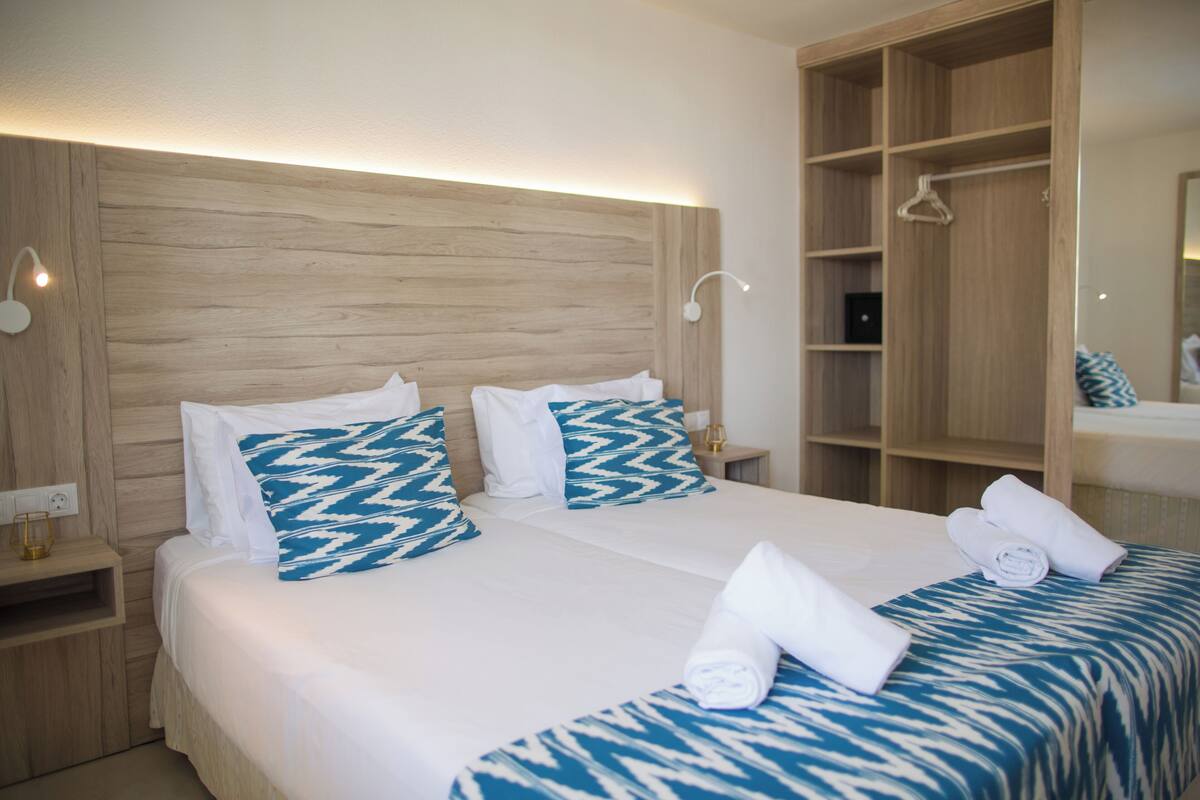 Ein Hotelzimmer mit einem Holz-Kopfteil, zwei Betten mit gemusterten Bettbezügen, einem Kleiderschrank und einem Spiegel.
