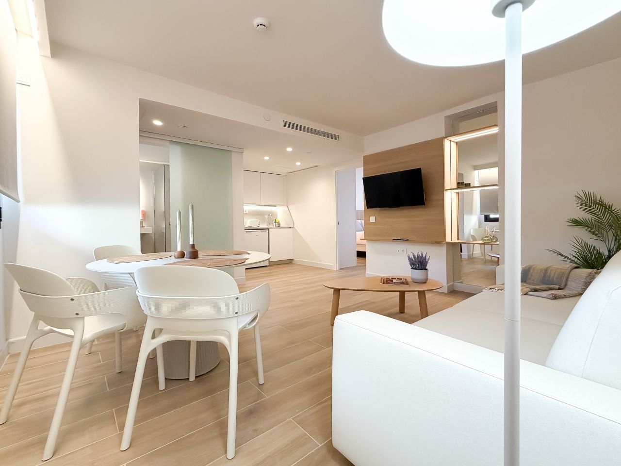 Un salon moderne avec un canapé blanc, une table à manger avec des chaises et un téléviseur fixé au mur.
