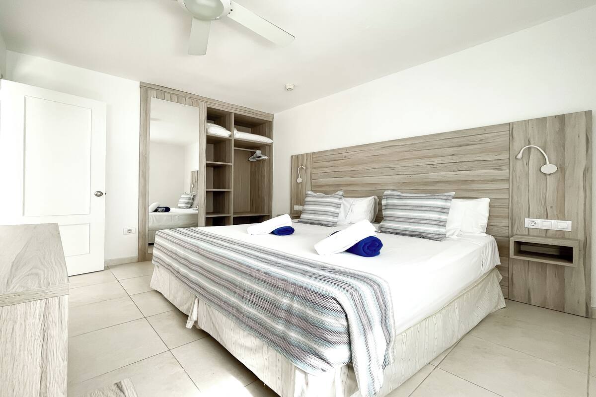 Ein Schlafzimmer mit einem großen Bett, einem Kleiderschrank, einem Nachttisch und einem Deckenventilator.