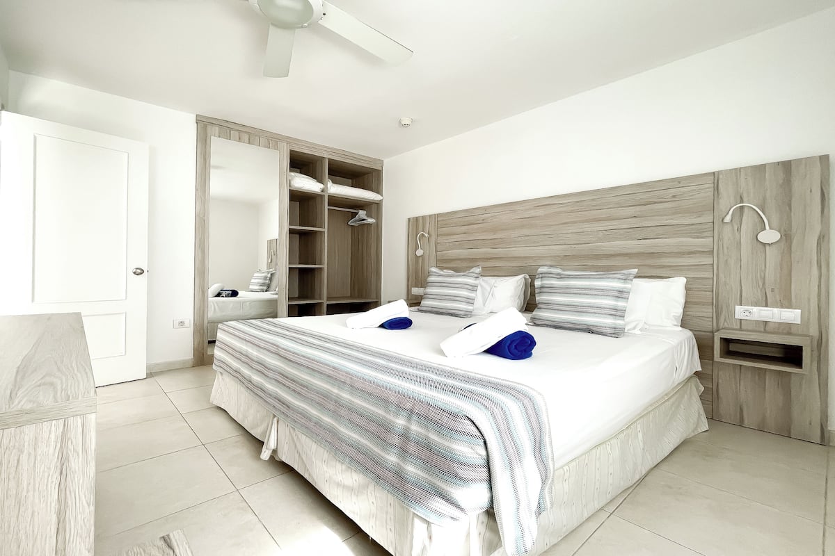 Ein Schlafzimmer mit einem großen Bett, einem Kleiderschrank, einem Nachttisch und einem Deckenventilator.