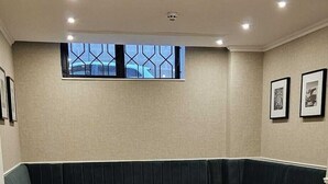 A modern hotel lobby with a herringbone wooden floor, a dark green upholstered bench seating area, and framed artwork on the walls. - Carlton Hotel (Sliema)