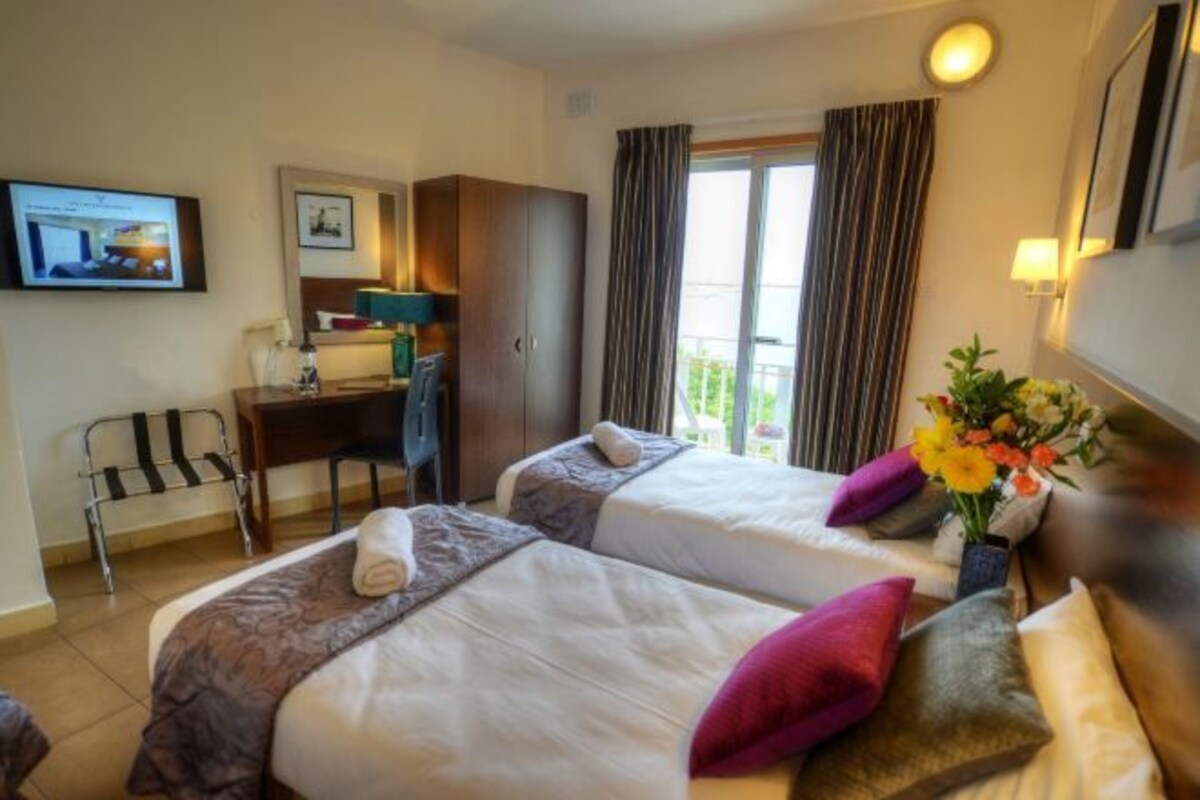 A hotel room with two beds, a desk, a chair, and a TV on the wall.