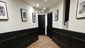 A hotel hallway with a herringbone-patterned wooden floor, black wainscoting, and framed pictures on the walls. - Carlton Hotel (Sliema)