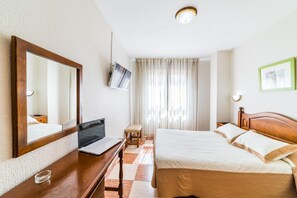 A hotel room with a wooden bed, a desk with a laptop, a mirror, a television, and a window with curtains.