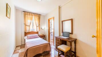 A bedroom with a bed, a desk with a laptop, a chair, and a mirror.