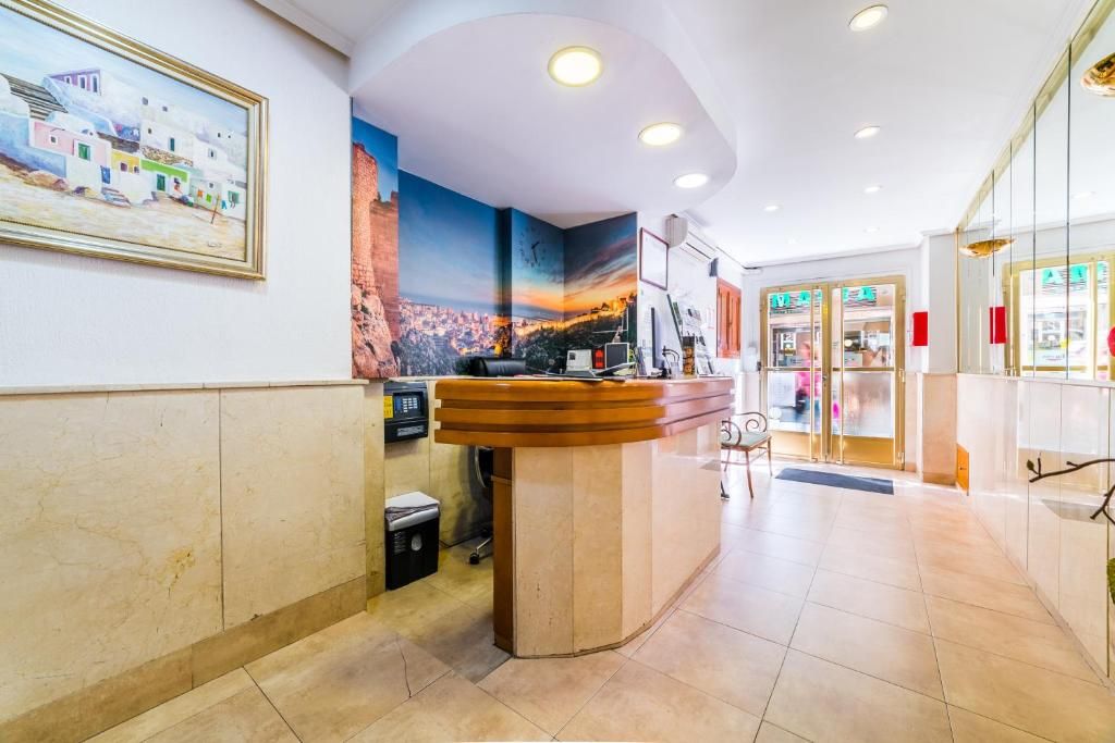 Un hall d’hôtel avec un comptoir d’accueil, un tableau représentant un paysage côtier et une vue sur le paysage urbain par la fenêtre.