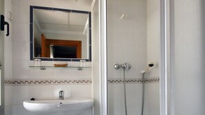 A bathroom with a white sink, a mirror, a shower enclosure, and a blue trash bin. - Hotel Sevilla (Almeria)