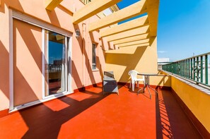 A balcony with a red floor, a glass door, a table with chairs, and a green railing.