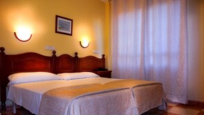 A hotel room with a double bed, two bedside tables, a nightstand, and a window with a curtain. - Hotel Sevilla (Almeria)