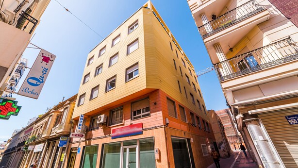 A multi-story hotel with a yellow facade, large windows, and a red awning. - Hotel Sevilla (Almeria)