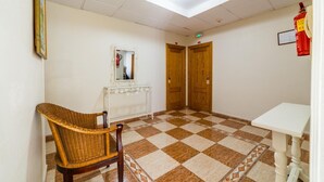 A hallway with a checkered floor, a wicker chair, a white table, and two wooden doors. - Hotel Sevilla (Almeria)