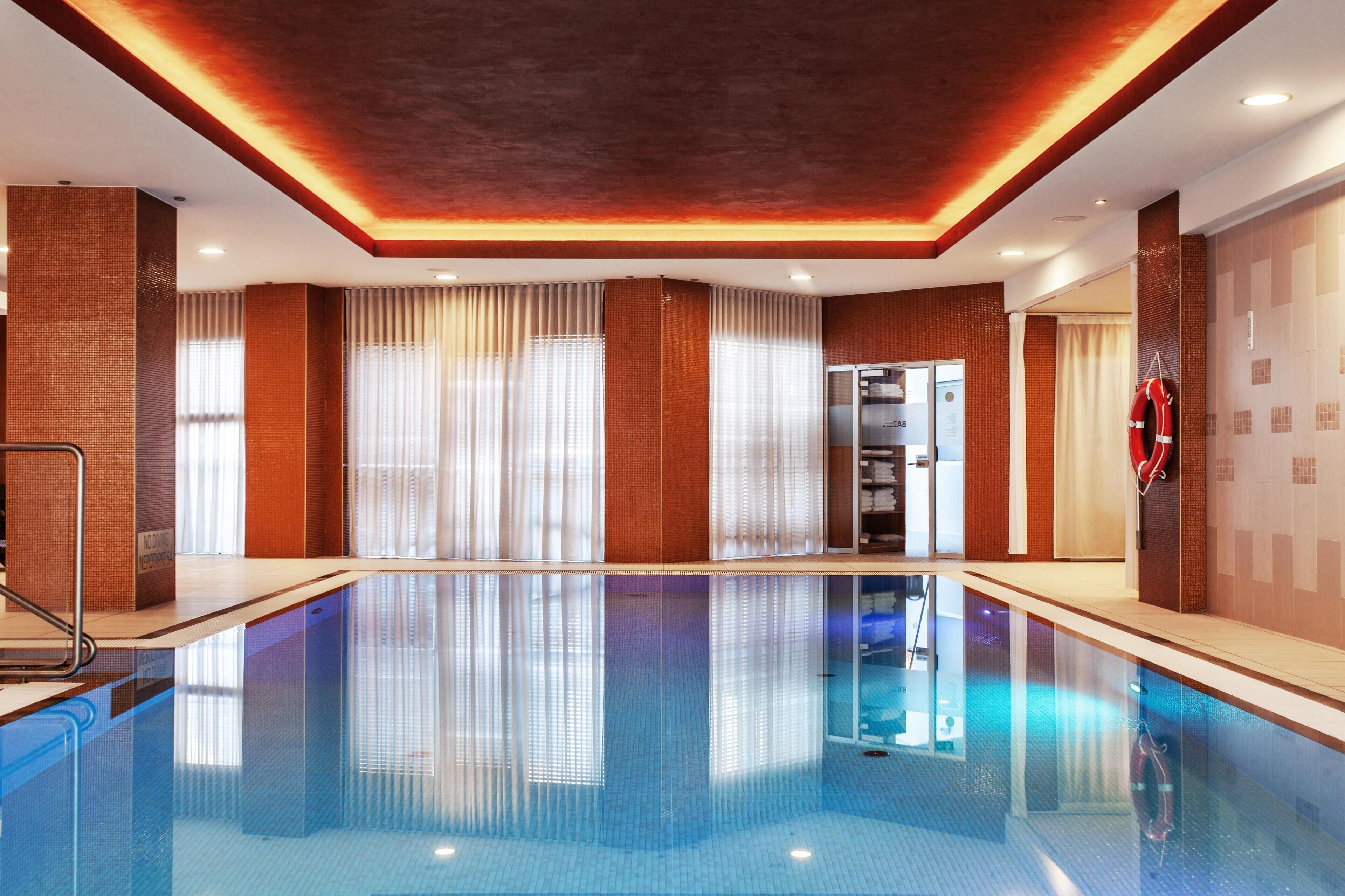 A swimming pool with a tiled floor, a diving board, and a lifebuoy on the wall.
