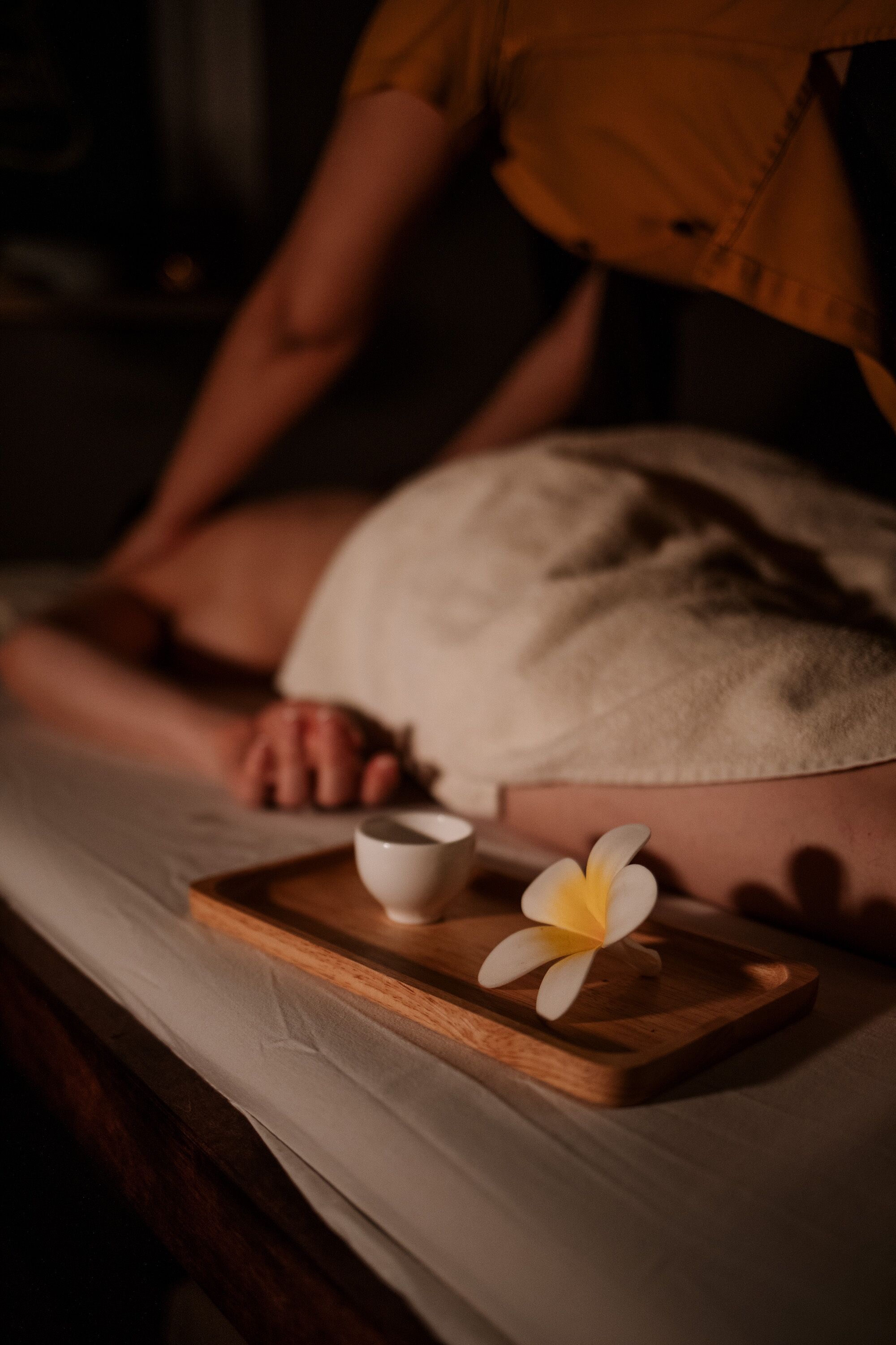 Una persona sdraiata su un letto con un asciugamano, un vassoio con un fiore e una tazza.