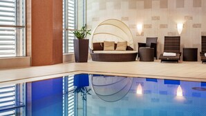Un área de piscina interior moderna con zona de estar, sillones reclinables y un ventanal grande.