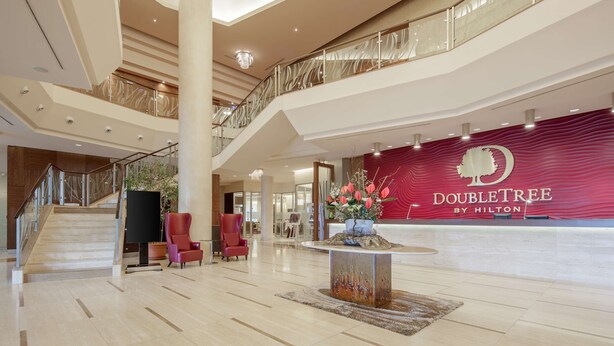 Un vestíbulo amplio con una imponente escalera, una mesa de recepción y una pieza decorativa central.