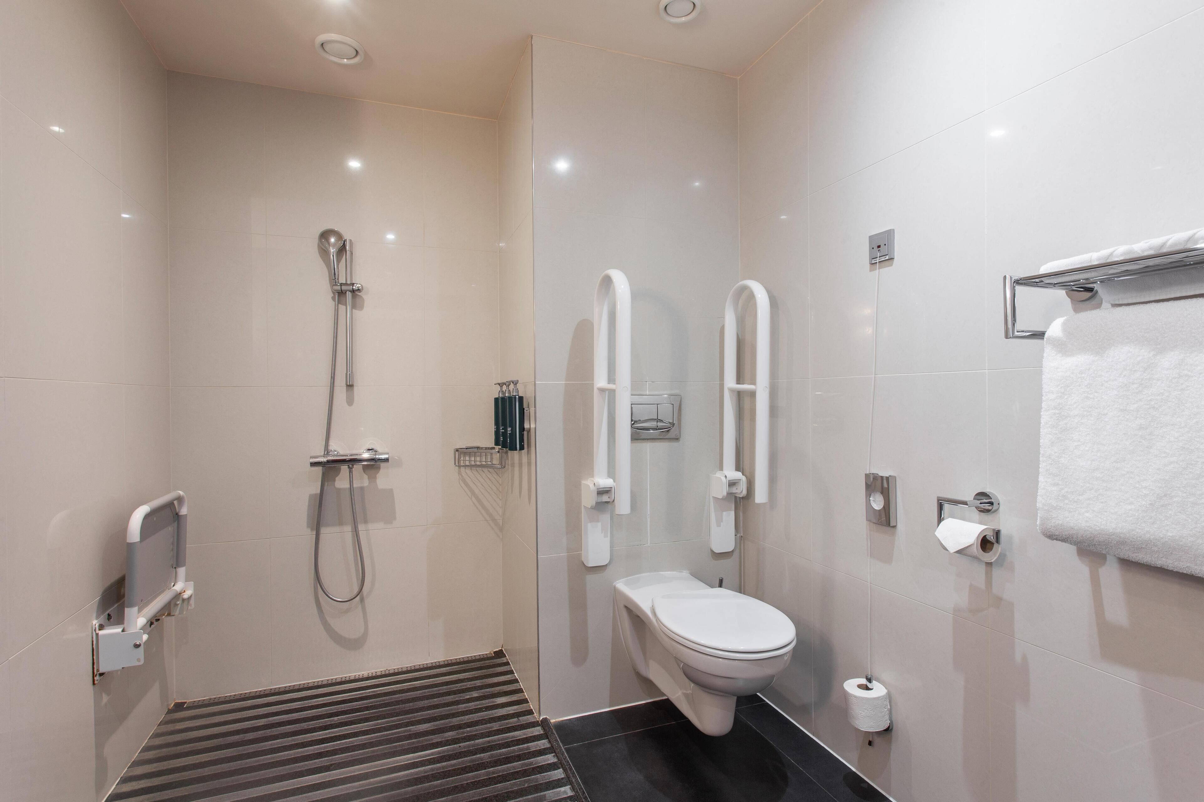 Un baño moderno con ducha, inodoro y barras de apoyo.