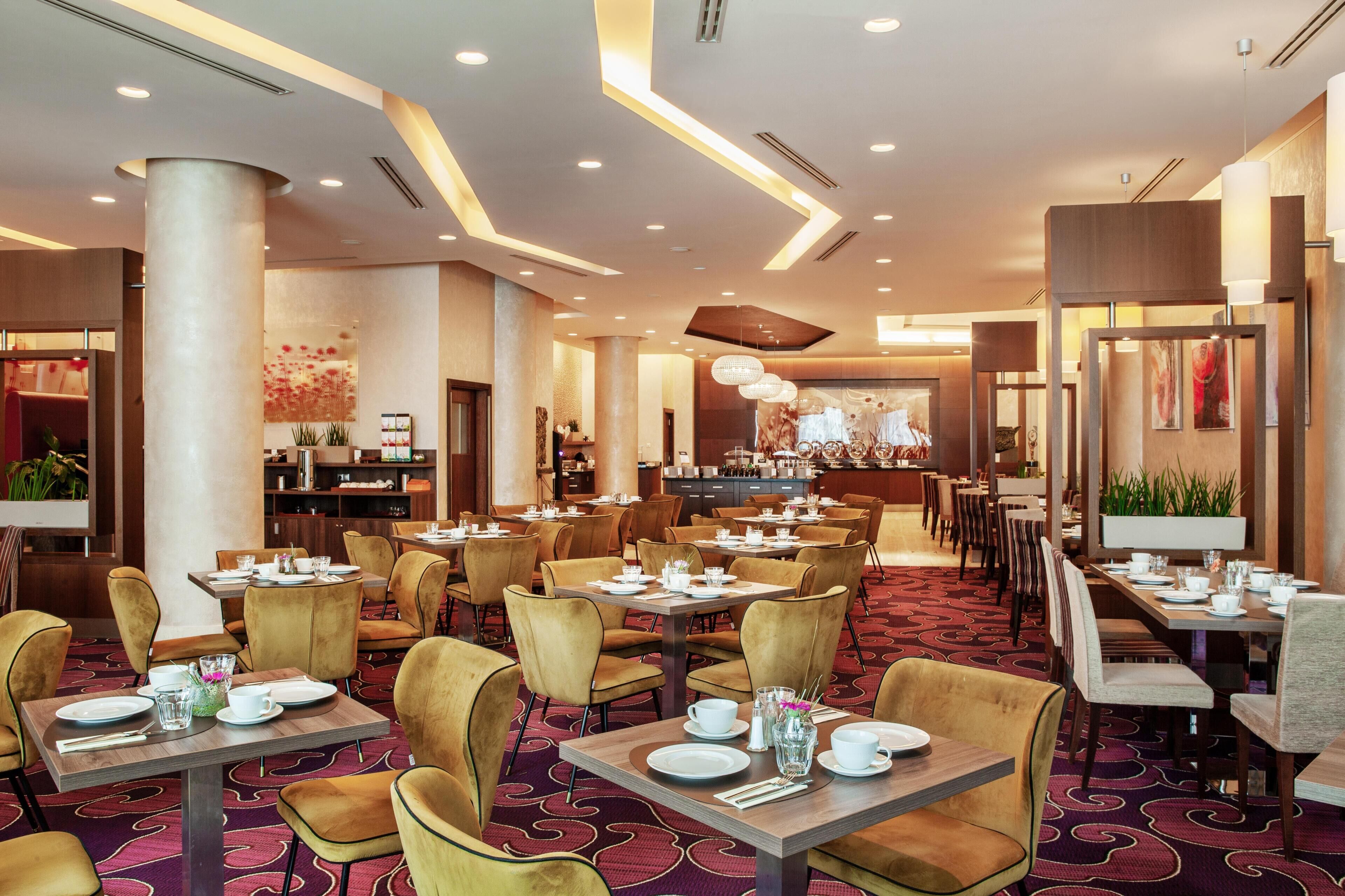 A hotel dining area with multiple tables and chairs, a central bar, and a patterned carpet.