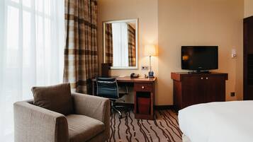 A hotel room with a bed, a desk with a chair, a television, and a window with curtains.